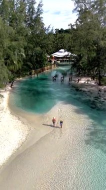 İki gezgin Koh Kood Adası 'nın kumlu sahilinde huzurlu bir yürüyüşün tadını çıkarıyor. Kristal berrak sular güneşin altında parıldıyor, yemyeşil ve Tayland 'da sakin bir atmosferle çevrili.
