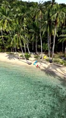 Tayland 'daki Koh Kood Adası' nın kumlu sahillerinde rahatlayın. Sakin suların, bereketli palmiyelerin ve güzel sahil şeridinin tadını çıkar. Sahilde yürüyen bir çift adam ve bir kadın.