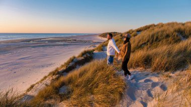 Uzun otlarla çevrili yumuşak kumullarda bir çift, Danimarka 'nın Blokhus Strand şehrinde altın saat boyunca Kuzey Denizi' nin sakin dalgalarını seyrediyor.