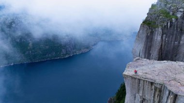 Preikestolen Cliff 'ten nefes kesici manzarayı keşfedin, Lysefjord' un aşağıdaki dramatik manzarasını ortaya çıkarın. Yalnız bir yürüyüşçü, gizemli sis ve dingin suların ortasında doğayı kucaklıyor..