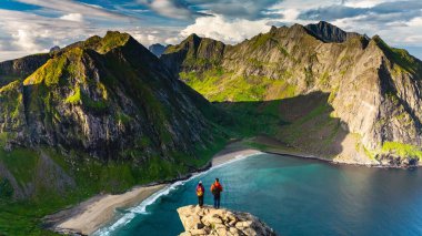 İki yürüyüşçü kayalık bir çıkıntıda durup Ryten Kvalvika Sahili 'nin büyüleyici manzarasına bakıyorlar..