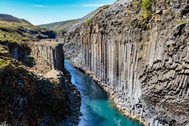 Studlagil Kanyonu 'nun çarpıcı özelliklerini keşfedin, kristal berrak suyun bazalt sütunlar arasında aktığı. Doğa meraklıları İzlanda 'nın engebeli arazisi boyunca yürüyüş yaparlar.