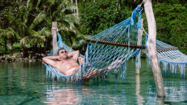 Tayland 'ın Koh Kood Adası' ndaki sakin suların üzerinde asılı duran canlı bir hamakta bir adam yatıyor. Yeşillik ve palmiye ağaçlarıyla çevrili bu sakin yer rahatlamaya ve huzura davet ediyor..