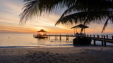 Nefes kesen gün batımı Koh Kood Adası 'nın sakin sularına altın bir ışık saçıyor. Çadırı olan büyüleyici bir iskele, palmiye ağaçlarının arasında dinlenmeye hazır..