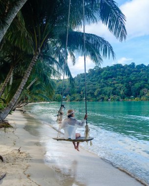 Sessiz bir sahilde salıncaktan keyif alan bir kadının sakin sahnesi. Etrafı gür palmiyelerle çevrili. Berrak turkuaz sular canlı yeşilliği yansıtarak Koh Kood Adası 'nda sakin bir atmosfer yaratıyor..