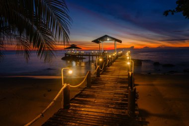 Tayland 'daki Koh Kood Adası' nda gün batımında resim gibi bir manzara gözler önüne seriliyor. Günbatımının ılık renkleri sakin suları yansıtıyor, ahşap iskeleyi aydınlatıyor..