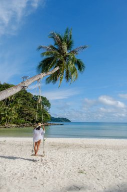Koh Kood Adası 'nda sakin bir sahnede yumuşak beyaz kumda palmiye ağacının altında sallanan bir kadın görülüyor. Sakin turkuaz sular ve yemyeşil yemyeşil Tayland 'da barışçıl bir tropik kaçış yaratır.