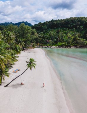 Koh Kood Adası 'ndaki güzel bir plajda beyaz kumlar ve gür palmiye ağaçları bulunur. Yumuşak dalgalar yavaşça kıyıya vuruyor Tayland 'da bir palmiye ağacının altında salıncakta sallanan bir çift erkek ve bir kadın.