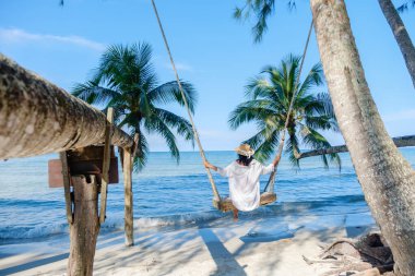 Asyalı bir kadının sallanan palmiye ağaçları ve dingin dalgalarla çevrili sahilde salıncaktan keyif aldığı sakin bir sahne Koh Kood Adası 'nda sergileniyor. Tayland