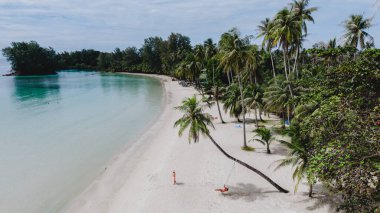 Koh Kood Adası 'ndaki sakin plajda yumuşak beyaz kum ve berrak mavi sular bulunur. Ziyaretçiler tropikal güneşin altında dinlenirken palmiye ağaçları rüzgarda hafifçe sallanıyor. Tayland 'da mükemmel bir kaçış.