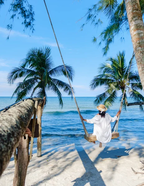 Koh Kood Adası 'nda, Tayland' da sakin bir plajda, Asyalı bir kadının salıncakta sallanmaktan zevk aldığı huzurlu bir manzara gözler önüne seriliyor.