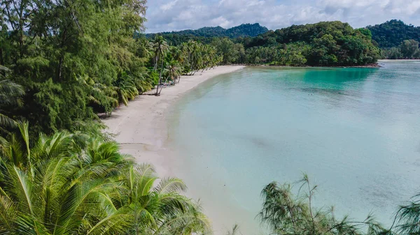 Tayland 'ın Koh Kood Adası' ndaki sakin bir plajın çarpıcı manzarası. Yumuşak beyaz kum kristal berrak sularla karşılaşır, yemyeşil palmiyeler parlak mavi bir gökyüzünün altında rüzgarda sallanır..