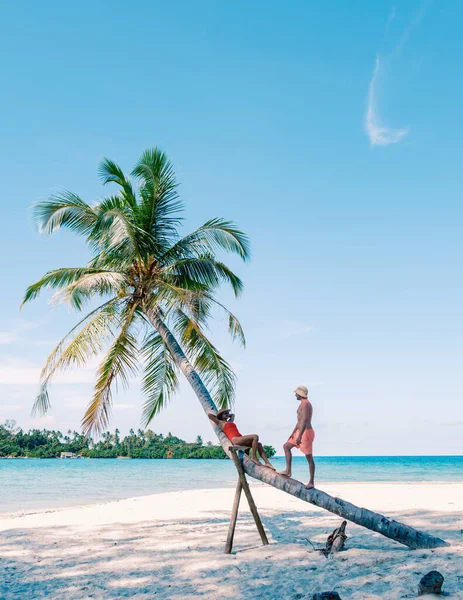 Tayland, Koh Kood 'daki güzel plaj sahnesinde bir kadının palmiye ağacına yaslandığı ve erkeğin bir çift olarak katılmaya hazırlandığı huzurlu bir an var..