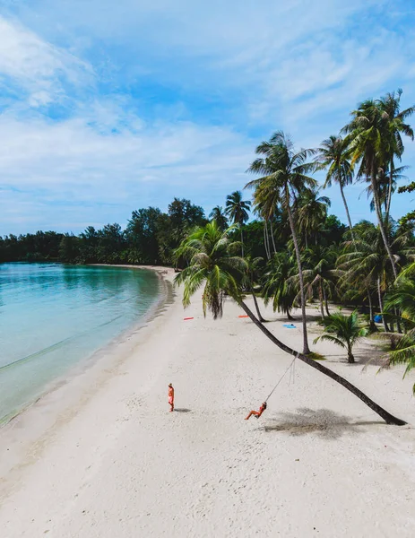 Ziyaretçiler Tayland 'daki Koh Kood Adası' nın huzurlu güzelliğinin tadını çıkarıyorlar. Yumuşak kumlar ve palmiye ağaçları rüzgarda hafifçe sallanıyor. Plajda palmiye ağacının altında sallanan bir çift.