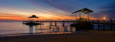 Gökyüzünün canlı renklere dönüştüğü Koh Kood Adası Tayland 'da nefes kesici bir günbatımının tadını çıkar. Sakin sular manzaralı rıhtıma çarpar ve huzurlu bir akşam ortamı yaratır..