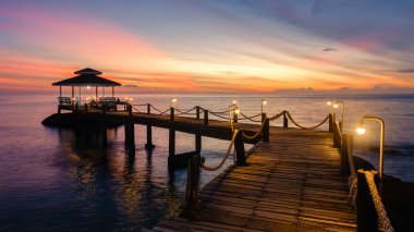 Güneş Koh Kood Adası 'nın sakin sularında batarken, ahşap bir iskelede rahatlayın. Gökyüzü turuncu ve pembe renkli canlı renklerle dolu. Tayland 'da bir akşam inzivası için güzel bir zemin hazırlıyor.