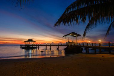 Nefes kesen bir günbatımı Koh Kood Adası 'ndaki sakin bir plajın üzerinde gökyüzünü canlı renklerle boyuyor. Ahşap bir iskele büyüleyici bir kulübeye götürür. Rahatlamak için ideal sakin bir atmosfer yaratır..
