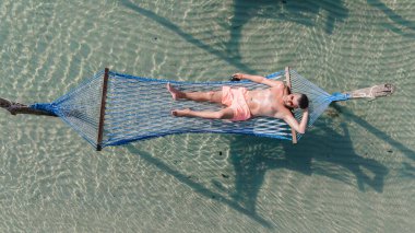 Bir adam Koh Kood Adası 'nın berrak turkuaz sularında asılı duran mavi bir hamakta vakit geçirmekten zevk alıyor. Huzurlu ortam Tayland güneşinin altında rahatlamaya ve sükunete davet ediyor.