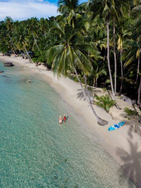 Tayland 'daki Koh Kood Adası' nda sakin bir sahilin nefes kesici manzarası. Ziyaretçiler, yükselen palmiye ağaçlarıyla çevrili güneşli gökyüzünün altındaki turkuaz suların tadını çıkarıyorlar. İdeal bir tropikal kaçış..