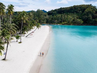 Tayland 'daki Koh Kood Adası' nın güzelliğini keşfedin. Yumuşak beyaz kumların turkuaz sularla buluştuğu yer. İnsanlar verimli yeşilliklerle çevrili kıyı boyunca huzurlu bir yürüyüşün tadını çıkarıyorlar..