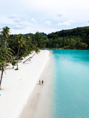 Yumuşak beyaz kumların turkuaz sularla buluştuğu Koh Kood Adası 'nın huzurlu güzelliğinin tadını çıkarın. Tayland 'da sahilde yürüyen bir çift kadın ve erkek.