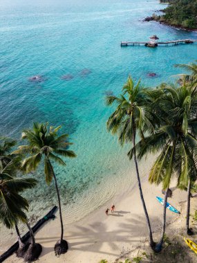 Çiftler, dalgalı palmiye ağaçları ve kristal berrak denizle çevrili Koh Kood Adası 'nın kumlu sahillerinde güneşli bir günün tadını çıkarıyorlar. Tayland 'da plaj boyunca kürek ve kanolar dinleniyor.