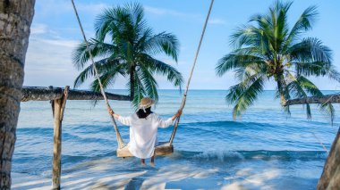 Bir kadın, Koh Kood Adası 'nın masmavi sularına bakan salıncakta sakin bir anın tadını çıkarır. Sabahın erken saatlerinde güneş dingin manzaraya sıcak bir parıltı yayarak tropikal cennet atmosferini güçlendirir..