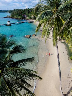 Tayland 'daki Koh Kood Adası' nın kumlu kıyılarında yürüyen iki kişinin çarpıcı hava görüntüsü. Bereketli palmiye ağaçları sahneyi çevreleyecek, sakin turkuaz sular güneşin altında rahatlamaya yol açacak..