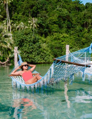 Bir kadın, Koh Kood Adası 'nın el değmemiş sularında asılı duran bir hamakta huzurun tadını çıkarıyor. Bereketli yeşillik, tropikal cenneti çevreleyip Tayland 'da sakin bir kaçış yaratır.