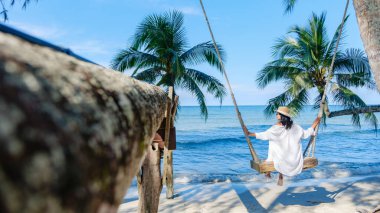 Koh Kood Adası 'nda sakin bir an. Bir kadın yumuşak kum ve berrak mavi sularda yavaşça sallanmaktan hoşlanıyor. Palmiye ağaçları hafif bir esintide sallanıyor, mükemmel bir tropik cennet yaratıyor Tayland 'da