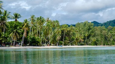 Koh Kood Adası 'nda bereketli palmiye ağaçları ve kumlu sahillerin olduğu huzurlu bir manzara. Ziyaretçiler deniz kenarında sakin bir günün tadını çıkarırlar. Bulutlu bir gökyüzünün altındaki güzellikler etrafını sarar..
