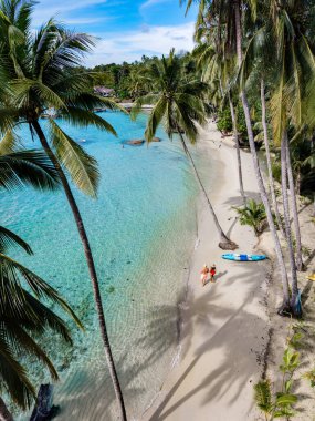 Dalgalar, sallanan palmiyelerle süslenmiş el değmemiş bir plaja çarpar. Kumsala giden iki kişi, güneşli bir günde Tayland 'ın Koh Kood Adası' nın doğal güzelliklerine bürünerek kıyı şeridinde gezerler..