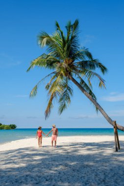 Bir çift, Koh Kood Adası 'nın yumuşak beyaz kumlarında el ele yürümenin keyfini çıkarıyor. Turkuaz sular ve sallanan palmiye ağaçları dinlenmek için mükemmel, sakin bir tropikal cennet yaratır..