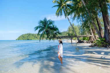 Tayland 'ın Koh Kood Adası' nda güzel kumlu bir sahil. Durgun bir kadın kristal berrak sularda duruyor. Etrafı gür palmiye ağaçları ve parlak mavi gökyüzünün altında canlı yeşilliklerle çevrili..