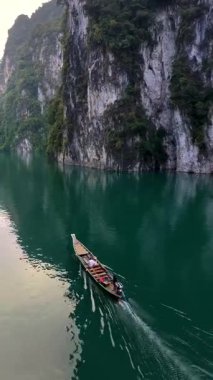 Tayland, Khao Sok 'un nefes kesici güzelliğini keşfedin. Büyüleyici kireçtaşı oluşumları ve yemyeşil alanlarla çevrili kristal berrak sularda süzülen geleneksel bir uzun kuyruklu tekne..