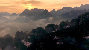 Tayland 'da Khao Sok Ulusal Parkı' nı aydınlatan büyülü gündoğumunu yaşayın. Sis yemyeşil dağların üzerinden yükselir, şafak vakti dingin ve büyüleyici bir manzara yaratır. Doğanın güzelliği gözler önüne seriliyor.