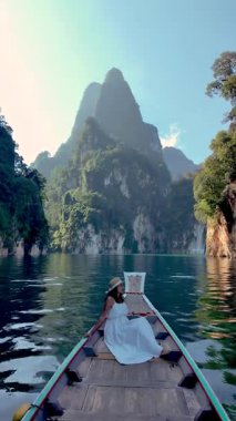 Tayland, Khao Sok 'un nefes kesici manzaralarını keşfedin, Asyalı bir kadın, büyüleyici dağlarla çevrili bir teknede dinlenirken ve parlak bir gökyüzü altında sakin sularda..