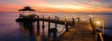 Tayland 'daki Koh Kood Adası' nın sakin cazibesini deneyin. Güneş sakin okyanus sularının üzerinde batarken. Lambalı ahşap bir iskele huzur dolu sahneyi aydınlatıyor. Rahatlamaya davet ediyor..