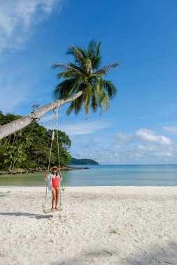 Bir kadın, Koh Kood Adası 'nın el değmemiş sahilindeki bir palmiye ağacının altında güneşli bir günün tadını çıkarıyor. Turkuaz sular ve yumuşak beyaz kum Tayland 'da mükemmel bir tropikal kaçış yaratır.