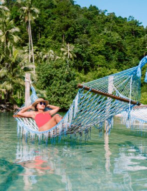 Koh Kood Adası 'nda bir kadının hamakta dinlenirken sakin suların keyfini çıkardığı sakin bir sahne. Bereketli yeşilliklerle çevrili, güneşin sıcaklığının tadını çıkartıyor, Tayland 'da rahatlamanın somutlaştırıcısı.