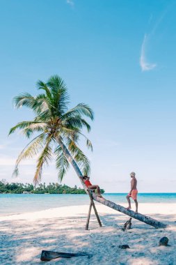Çeşitli bir çift, uzun palmiye ağaçları ve parlak turkuaz sularla çevrili Koh Kood Adası 'ndaki sakin plajda eğleniyor. Sıcak güneş Tayland 'daki tropik cennet atmosferini güçlendiriyor.