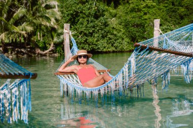 Huzurlu bir sahnede Koh Kood Adası 'ndaki berrak suların üzerinde bir hamakta uzanan bir kadın görülüyor. Yeşilliklerle çevrili bu dinlendirici ortam, doğal güzellikte gevşemek için mükemmeldir..