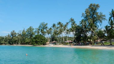 Parlak mavi sular Koh Kood Adası 'nın kumlu kıyılarına nazikçe çarpar. Ziyaretçiler güneşli bir günün tadını çıkarırken palmiye ağaçları rüzgarda sallanıyor. Ao Taphao Sahili