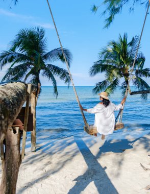 Tayland 'ın Koh Kood Adası' nda sakin denizi ve gür palmiye ağaçlarını gören bir kadının nazikçe sallanışını gösteren sakin bir an. Parlak gökyüzü huzurlu atmosferi güçlendirir..
