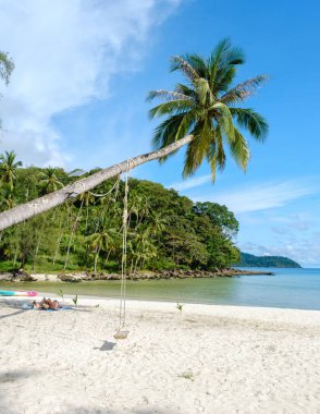 Ziyaretçiler, Tayland 'daki Koh Kood Adası' nda palmiye ağaçlarının gölgesinde huzurlu bir günün tadını çıkarıyorlar. Açık mavi gökyüzü el değmemiş kumlu plajlarla buluşur ve mükemmel bir tropik cennet manzarası yaratır..
