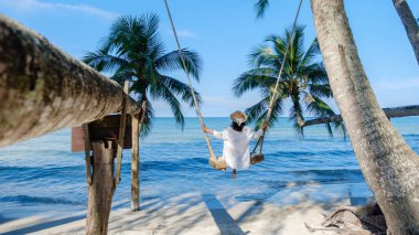 Koh Kood Adası 'ndaki sakin bir sahnede kırsal bir salıncakta hafifçe sallanan bir kadın görülüyor. Dalgalanan palmiye ağaçlarıyla çevrili, dalgalı mavi okyanus, rahatlamak için mükemmel sakin bir atmosfer yaratır..