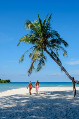 İki arkadaş Koh Kood Adası 'nda açık mavi gökyüzünün altında yumuşak beyaz kumlar üzerinde el ele yürüyorlar. Bereketli palmiye ağacı, turkuaz sulara doğru incelikle eğilir ve sakin bir tropik manzara yaratır..