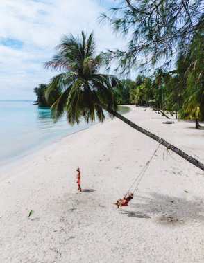 Kafkasyalı bir çift ve Asyalı bir kadın, Koh Kood Adası 'nda sakin bir günün tadını çıkarıyorlar. Yumuşak beyaz kumdaki bir palmiye ağacının altında sallanıyorlar. Durgun turkuaz sular ve yemyeşil yemyeşil sular.