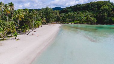 Ziyaretçiler Tayland 'ın el değmemiş Koh Kood Adası sahilinde huzurlu bir günün tadını çıkarıyorlar. Yumuşak kum ve berrak mavi sular dinlenmek ve keşfetmek için mükemmel sakin bir atmosfer yaratır..