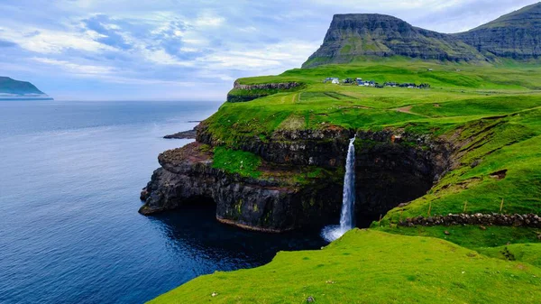 Gasadalur Şelalesi kayalık kayalıklardan Atlantik Okyanusu 'na yuvarlanırken. Yazın Mulafossur ve Gasadalur Köyü, Faroe Adaları